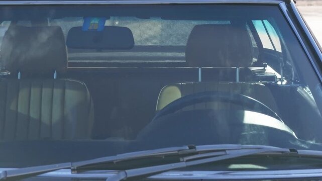 Front windscreen of a dark classic convertible showing tan leather seats, steering wheel and wipers in sunlight, French Riviera, France.