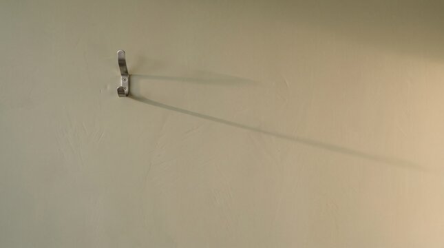 Single steel wall hook casting a long shadow on a pale olive wall