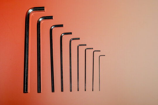 Set of metal hex keys neatly arranged in ascending size order on a bright orange and peach gradient background. Shiny chromed tools form a clear diagonal line and a minimalist composition.