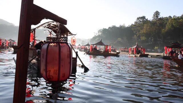 Decorative red Chinese lantern on a wooden post with tourists in traditional boats navigating a lake during a beautiful golden sunrise and morning, Ban Rak Thai, Mueang Mae Hong Son, Thailand.