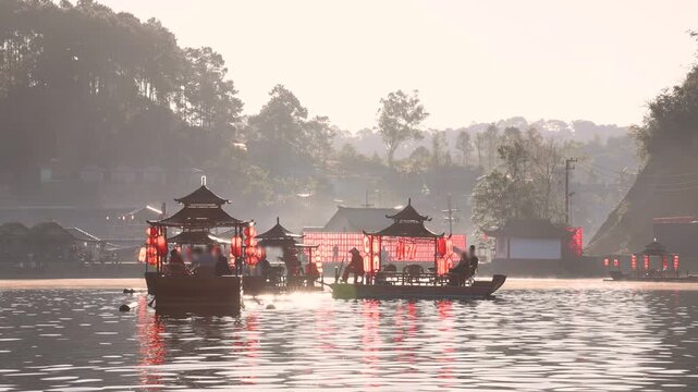 Traditional Chinese style boats decorated with red lanterns carrying tourists on peaceful lake during morning with golden sunlight and mountain landscape in Ban Rak Thai, Mueang Mae Hong Son, Thailand