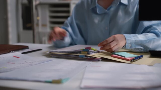 Office worker organizing a stack of printed financial documents with colorful index tabs on a desk, illustrating accounting administration, bookkeeping records, and business paperwork management.