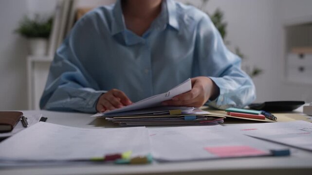 Business professional holding printed financial reports above an organized stack of documents, illustrating accounting review, bookkeeping verification, office administration, and record management.