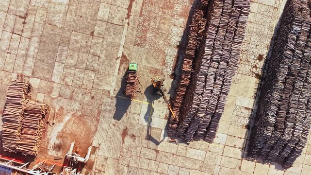 Workers move clay bricks through a brick storage yard with a small vehicle, seen from above during daylight; the location and date are not known.