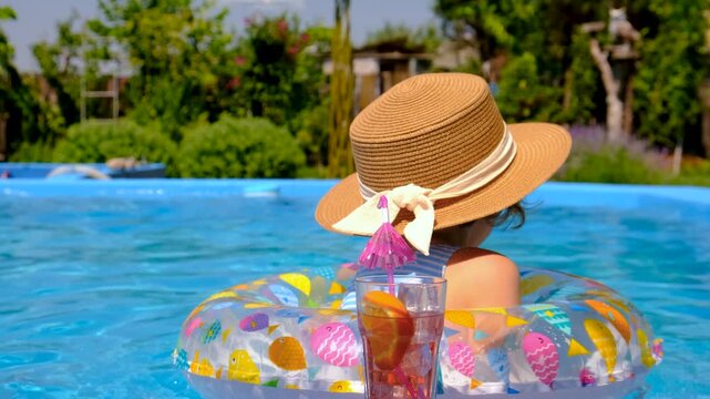 A child is drinking a cocktail by the pool. Selective focus.