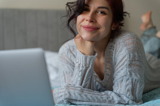 Smiling woman use laptop while relaxing in bed at home