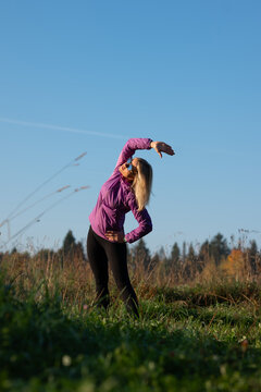 Woman perform side bend exercise outdoors under blue sky