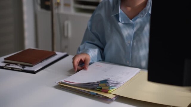 Office employee sorting financial paperwork inside a folder with colorful document tabs, illustrating accounting organization, bookkeeping administration, and professional business record management.