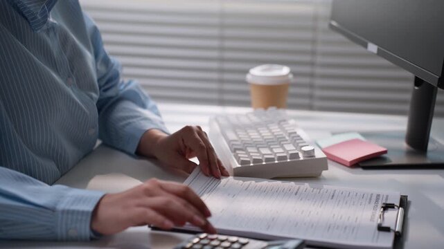 Office professional typing on a white keyboard beside printed financial documents and a calculator, representing accounting data entry, bookkeeping, digital administration, and business productivity.