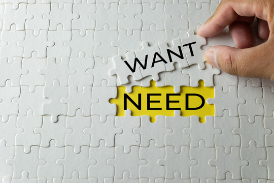 Hand placing a puzzle piece with the word WANT into a yellow missing space with the word NEED. Concept of psychological decision making, financial planning, desires versus necessities, and priority.