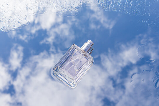 Clear fragrance bottle with raindrops against bright sky