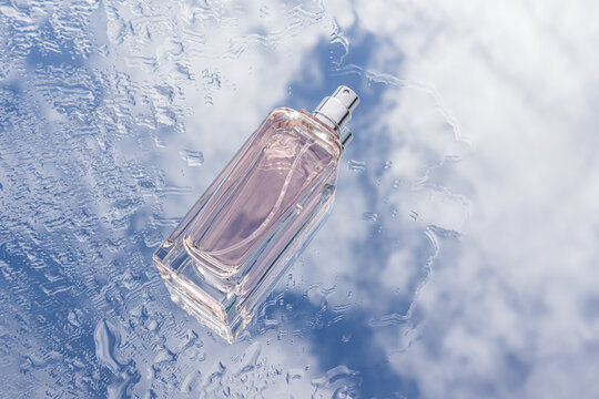 Perfume bottle with raindrops against bright cloudy sky
