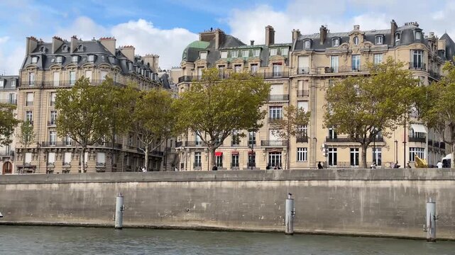 Historic Haussmann-style buildings line the Seine River in Paris, France, featuring ornate limestone facades, mansard roofs, and autumn trees. 15476  