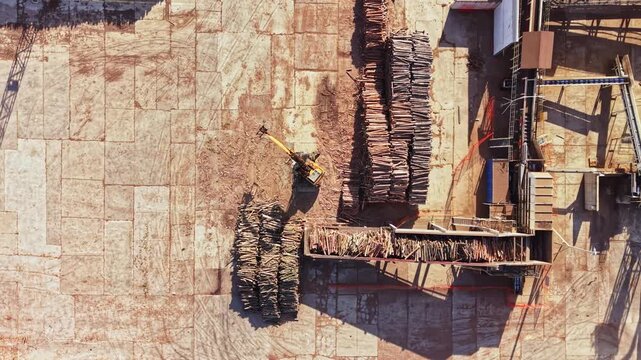 Workers use ropes and platforms to secure stacked timber panels against a large wall at a building construction site in daylight.