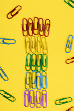 Colorful rainbow paper clip arrangement on yellow background