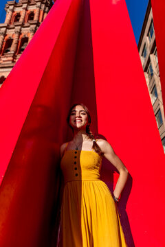 Mexican teenager in yellow dress beside red urban sculpture