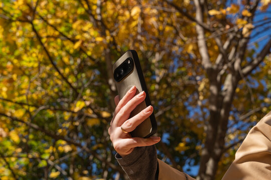 Woman hold smartphone in autumn park with blurred foliage