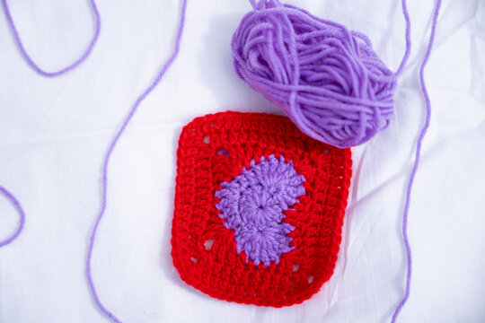 Red and purple crochet square with yarn ball