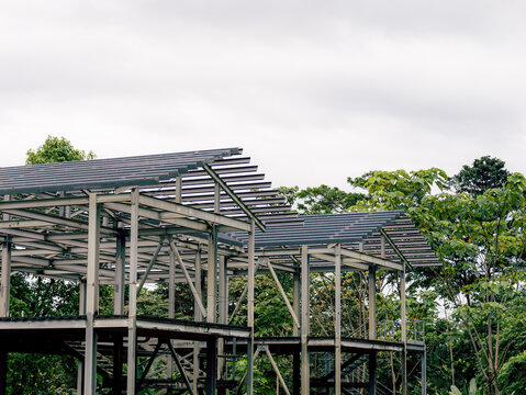 Steel framework construction beside forest under cloudy sky