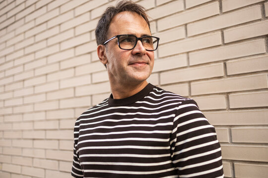 Mature man in striped shirt standing by brick wall