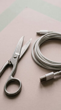 Steel Scissors Lying Beside Coiled White Electronic Charging Cable