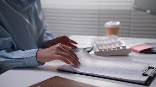 Office professional reviewing printed financial documents at a desk with a white keyboard and calculator, representing accounting analysis, business paperwork verification, and bookkeeping administrat