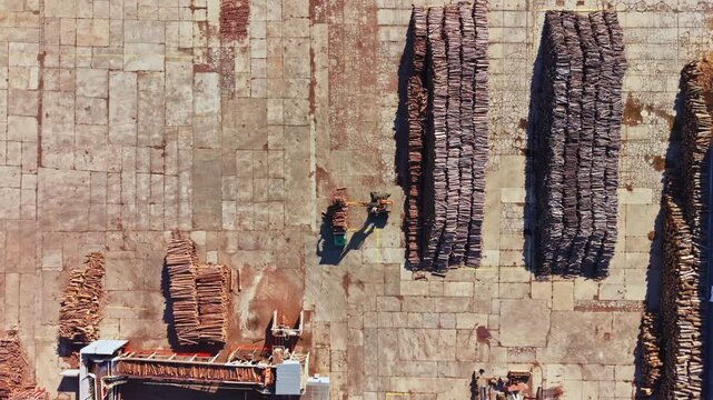 Workers arrange long bundles of reeds across a stone-paved work site, with stacked materials and equipment visible from above in daylight.