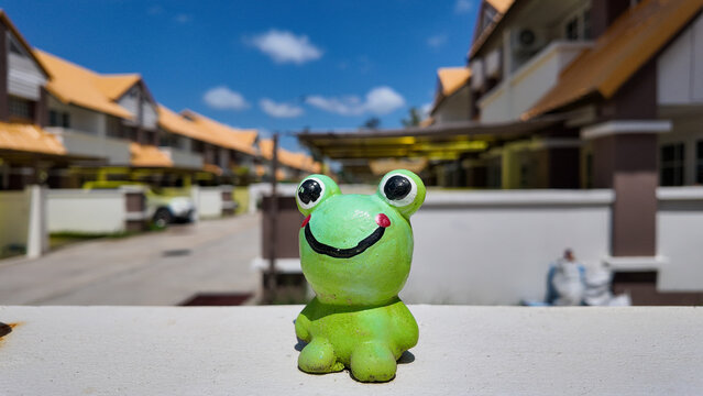 Cute Green Frog Figurine in Front of Residential Area on Bright Day