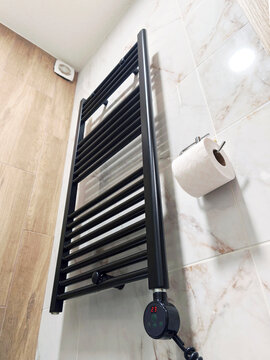 Black electric towel warmer rail with digital display on marble look ceramic tiles. Captures bathroom heating equipment, space-saving radiator fixture, energy smart drying, and supplementary room heat