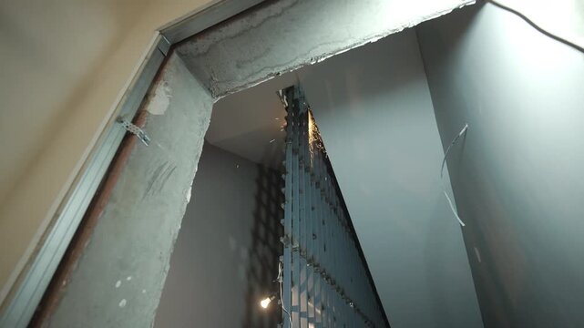 Metal grid door stands installed inside dark grey room opening. Industrial indoor environment highlights active interior finishing