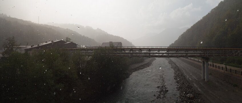 Panoramic view of river and bridge under rainy sky in mountain valley
