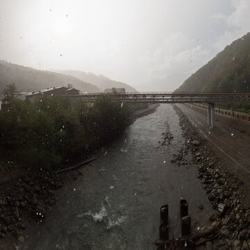 Mountain river with bridge and buildings during heavy rain