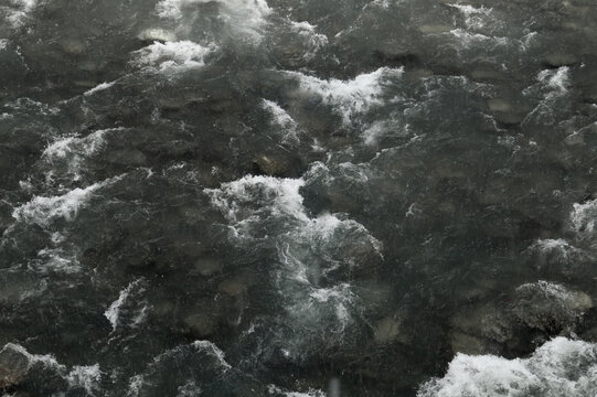 Top view of dark turbulent river water with white foam