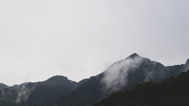 Dark mountain ridge with white fog against pale grey sky