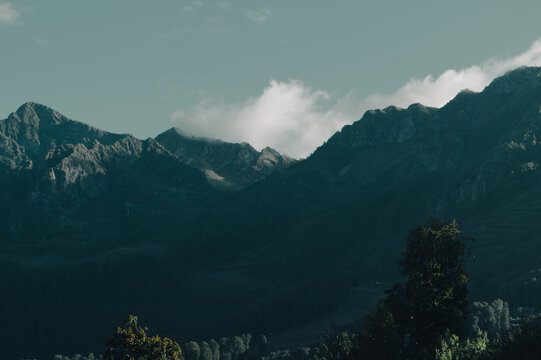 Dark mountain range with a single white cloud in a pale sky