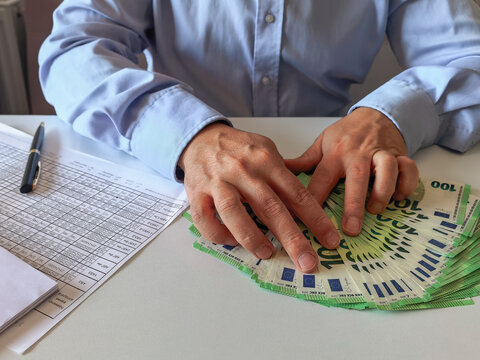 Top view of businessman counting stack of 100 euro banknotes at office desk.