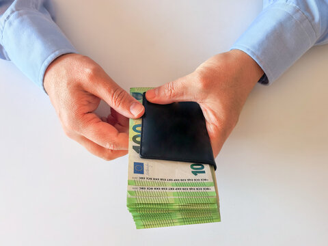 Man counting a stack of euro banknotes near a leather wallet.