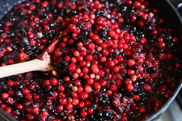 Traditional home-cooked lingonberry and forest blueberry jam cooking in a pot with a wooden spoon. © Silviu