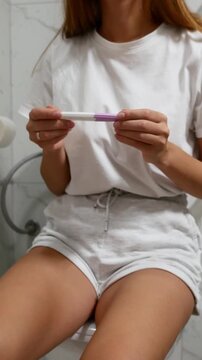 Close-up of woman holding pregnancy test while sitting in bathroom, home pregnancy testing and family planning concept.