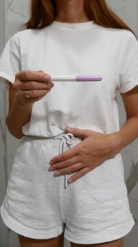Close-up of woman holding pregnancy test and touching stomach, concept of pregnancy, family planning and reproductive health
