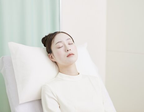 Young Japanese woman with a pale face resting with her eyes closed against a pillow on a clinic examination bed