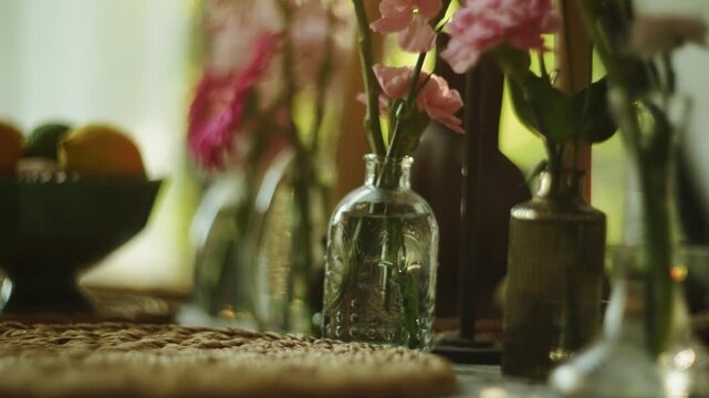 Pink flowers blooming inside small glass vases sitting on a table near a sunny window indoor