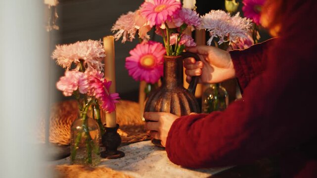 Close up of candles and pink flowers in glass vases on a dinner table during evening