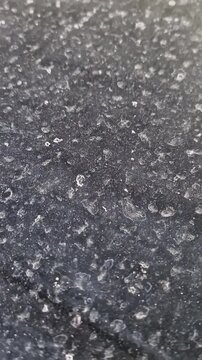 Water stain spots cover a dusty black surface with visible grimy residue buildup. Static macro framing captures dried mineral deposits and textured grime under soft overhead lighting.