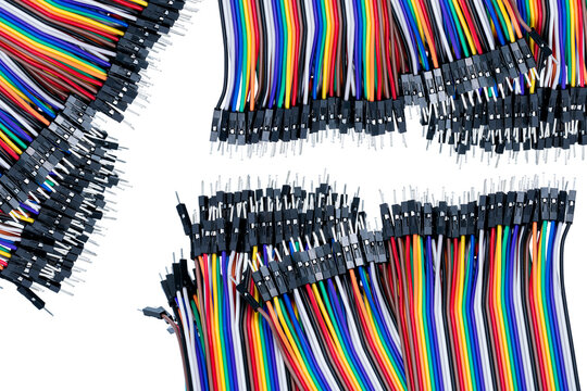 Multicolored jumper wires with male pin connectors arranged around white copy space, electronic cables for breadboard circuits, microcontroller prototyping, robotics and engineering projects