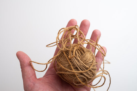 Hand holding ball of natural jute twine with loose loops, brown hemp string skein, rustic craft and eco packaging material