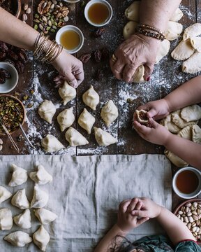 Overhead view of two pairs of diverse hands kneading and shaping rustic bread dough on a flour dusted wooden table