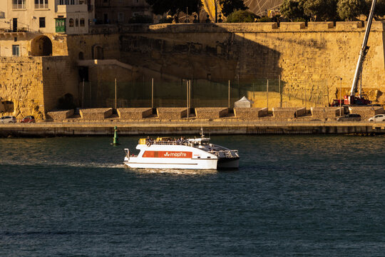 Valletta, Malta - October 14th, 2026 Passenger Ferry Catamaran On Calm Harbor Water Along Historic Stone Coastal Waterfront