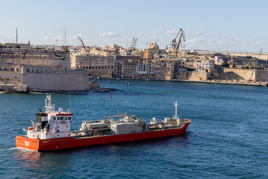 Valletta, Malta - October 14th, 2026 Red Cargo Ship Sailing Past Historic Fortifications in a Mediterranean Harbor Waterfront