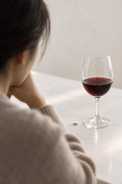 Red wine beside an antidepressant tablet with a person seated at a table. Alcohol use and medication interaction. Depression and addiction treatment awareness. Substance misuse concept.